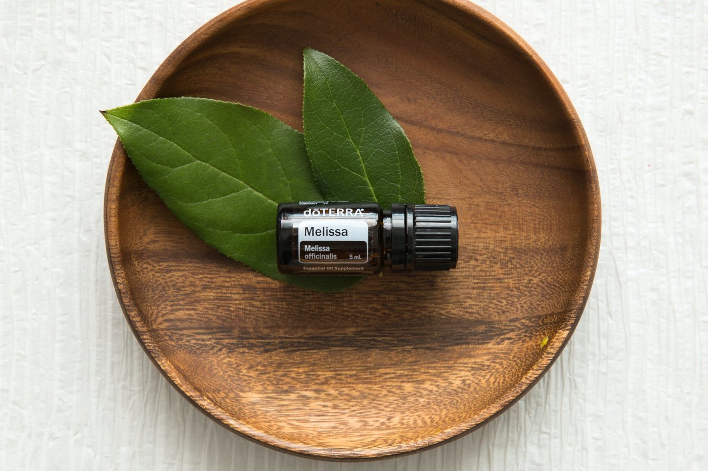 Sticluță dōTERRA Melissa pe o farfurie de lemn cu frunze