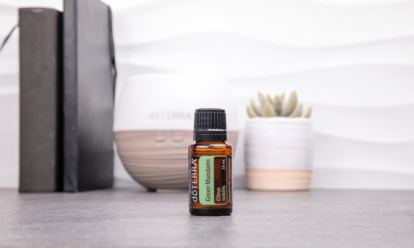 A dōTERRA bottle on a shelf in front of a white diffuser, with books and a small plant