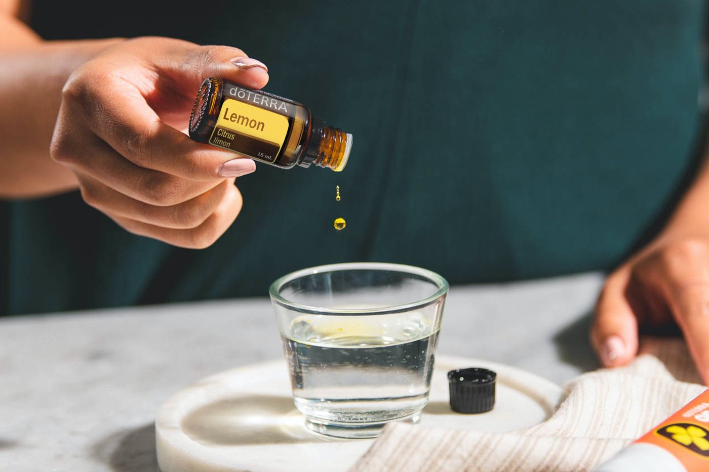 A drop of dōTERRA Lemon oil being added to a glass of water