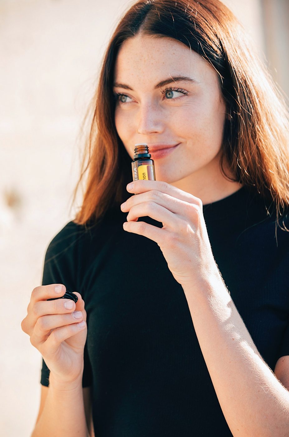Жінка в чорній футболці вдихає аромат олії dōTERRA з флакона