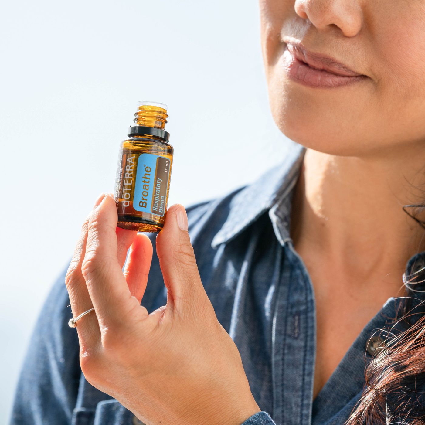 Lächelnde Frau in einem Jeanshemd hält eine kleine dōTERRA-Flasche in der Hand, Nahaufnahme