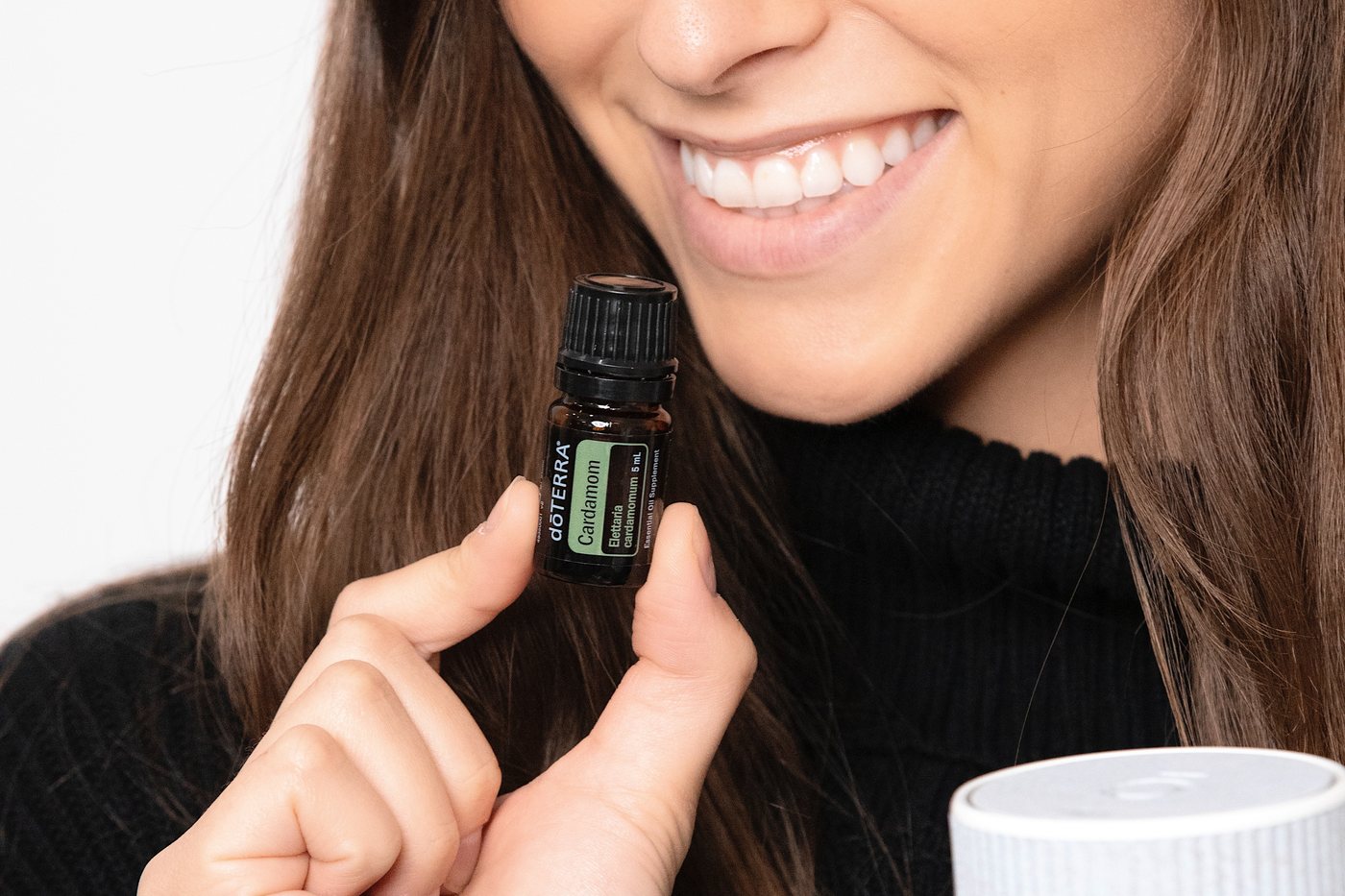 A smiling woman holding a dōTERRA bottle next to a diffuser